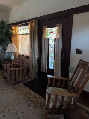 Ein Zimmer mit Holztür, einem Fenster mit Buntglas, einer Lampe und zwei Holzstühlen.