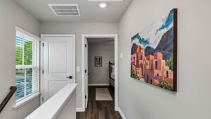 Un corridoio con una porta bianca, un quadro appeso al muro e un pavimento in legno.