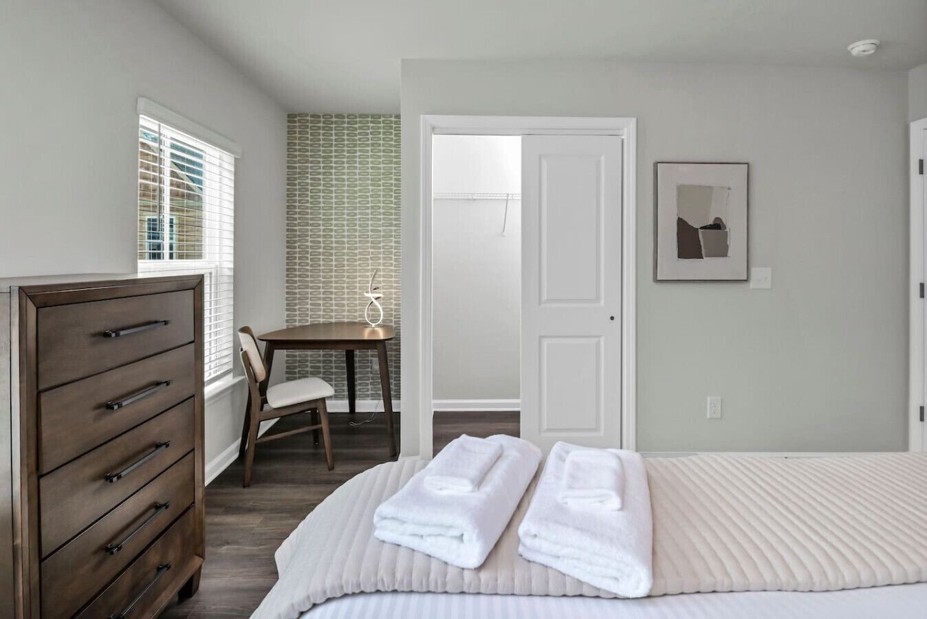A bedroom with a bed, a dresser, a chair, a table, and a door.