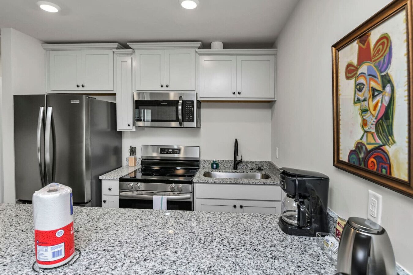 A modern kitchen with white cabinets, stainless steel appliances, granite countertops, and a coffee maker.