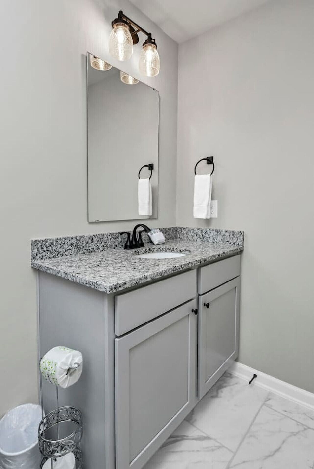 Une salle de bain avec un comptoir en granit, un lavabo, un miroir et un porte-serviettes.