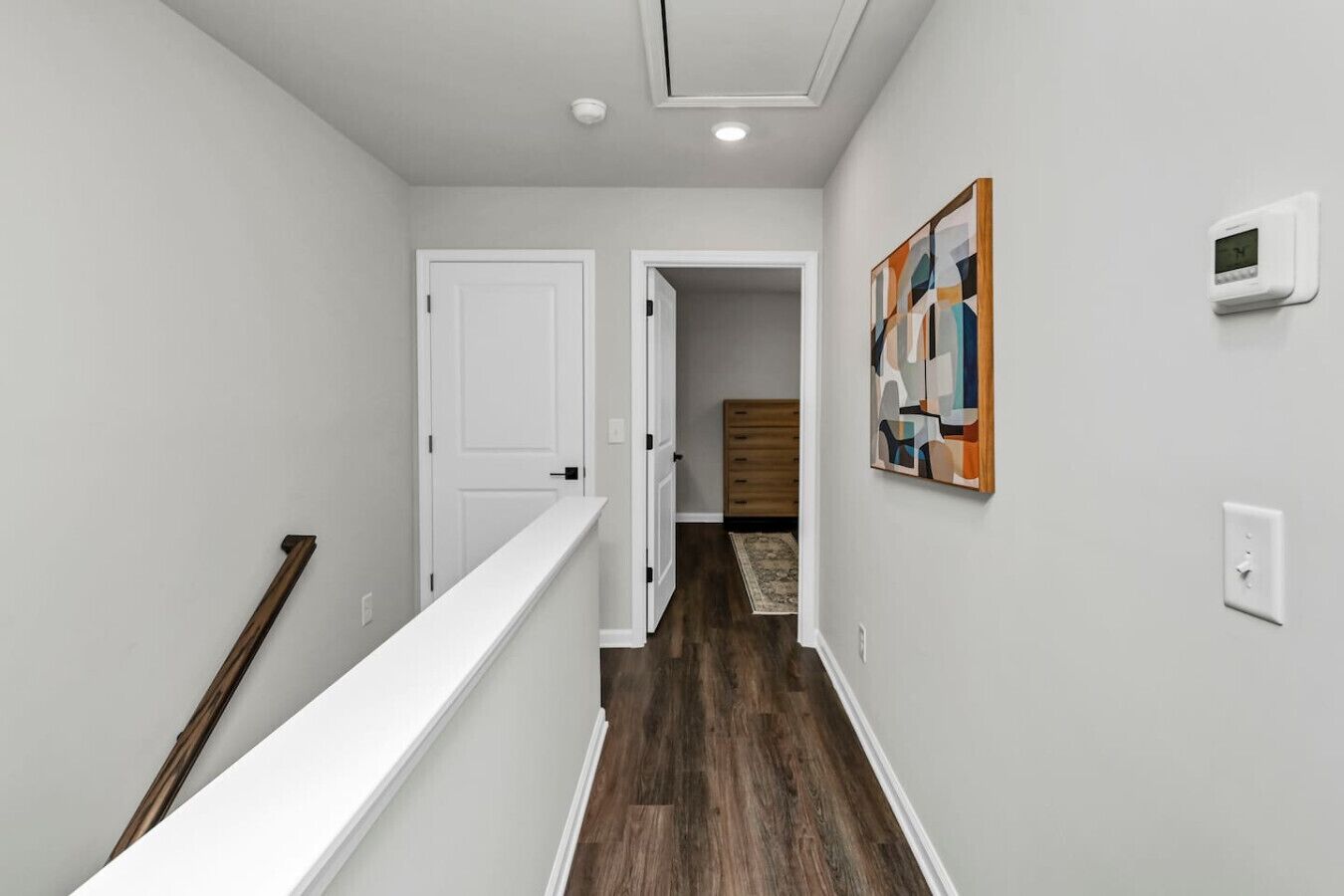 A hallway with a wooden floor, white walls, a white door, and a painting on the wall.