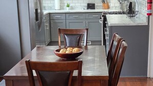 A modern kitchen with grey cabinets, a stainless steel refrigerator, a marble countertop, and a dining table with four wooden chairs. - Stunning Elmwood Village Lower  (Buffalo)