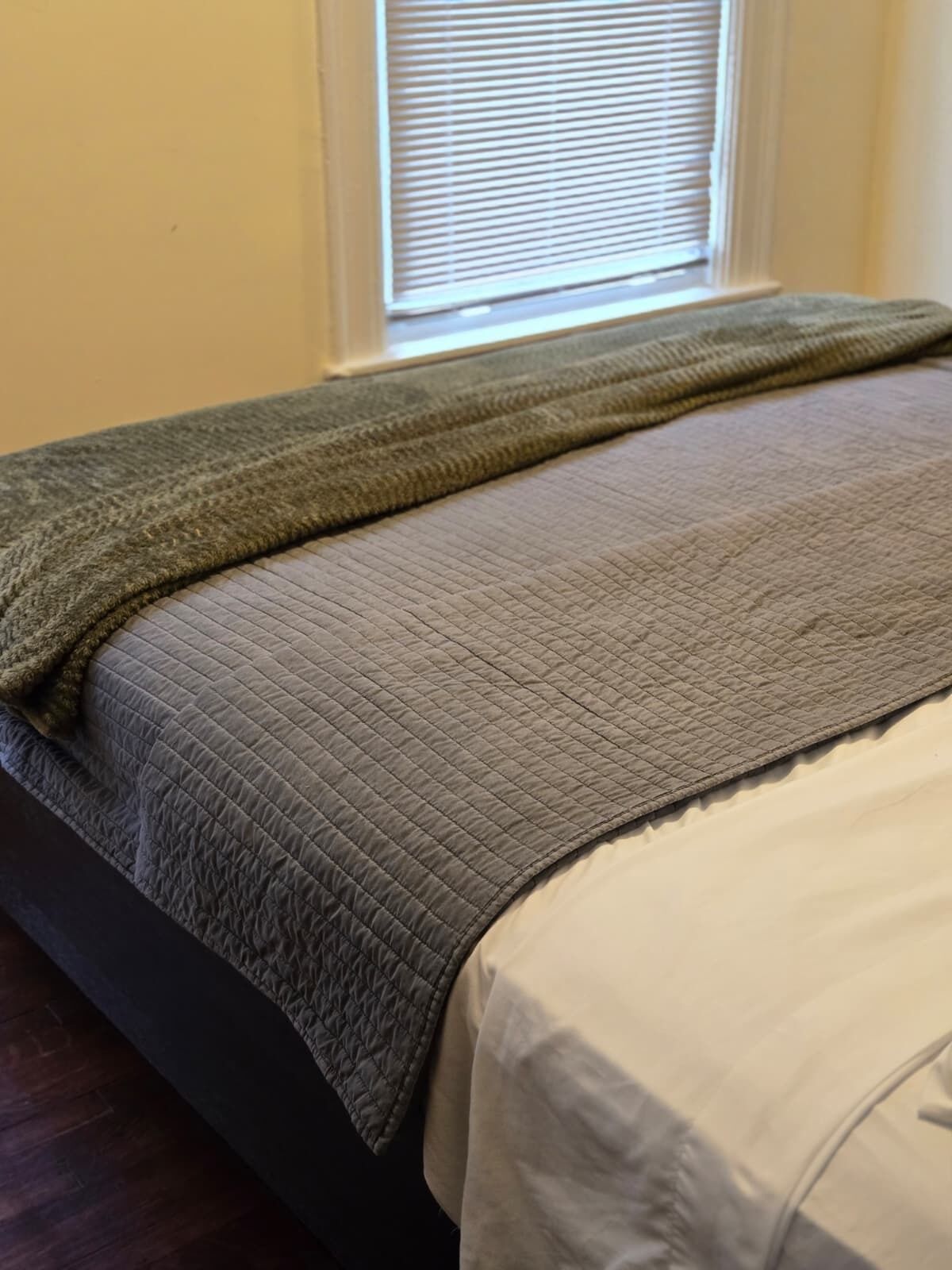 A bed with a quilted bedspread and a green blanket.