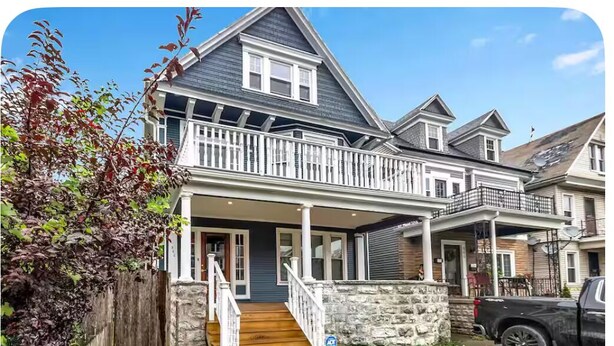 A two-story house with a porch, a stone wall, and a wooden staircase. - Stunning Elmwood Village Lower  (Buffalo)