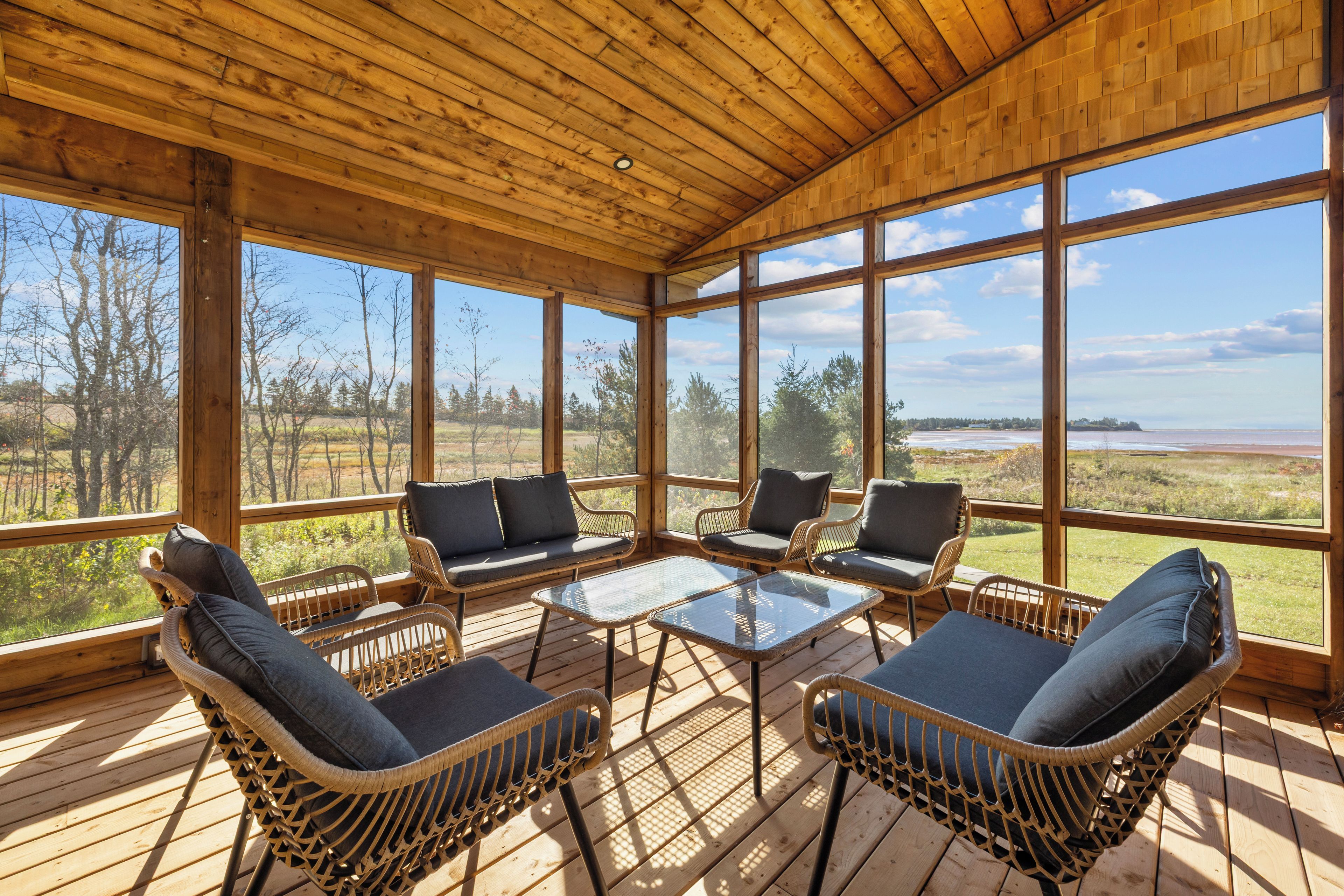 A wooden deck with wicker furniture and large windows offering a view of a natural landscape.
