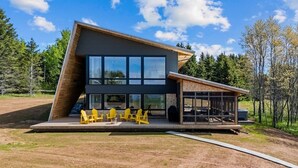 Ein modernes Haus mit großem Panoramafenster, einer Holzterrasse und Gartenmöbeln.