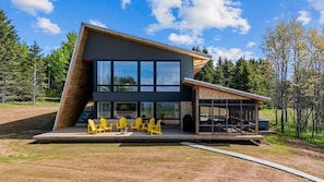 A modern house with a large glass window, a wooden deck, and outdoor seating.