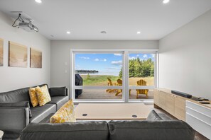 A modern living room with a gray sofa, yellow patterned pillows, a wooden coffee table, and a view of a deck with outdoor furniture.