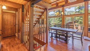 A wooden interior with a staircase, a dining table, and large windows. - Monthly Lease - Pine Trail at Alpine Meadows - Pet Friendly w Hot Tub at Alpine Meadows (Alpine Meadows)