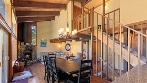 A spacious living area with a fireplace, wooden staircase, and a dining table with chairs. - Monthly Lease - Pine Trail at Alpine Meadows - Pet Friendly w Hot Tub at Alpine Meadows (Alpine Meadows)