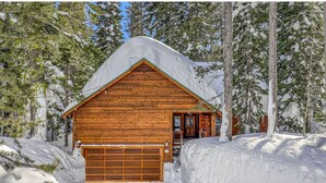 Eine Holzhütte mit Garage, umgeben von Schnee und Bäumen.