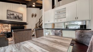 Une cuisine moderne avec des meubles blancs, une cheminée en pierre et un coin repas comprenant une table en bois et des sièges en cuir.