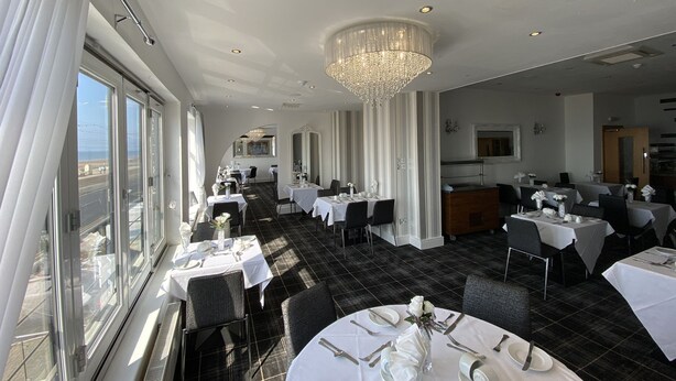 A restaurant with tables set for dining, a chandelier, and large windows.