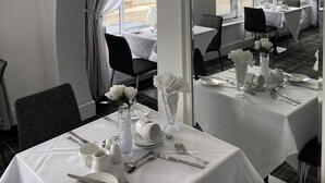 A dining area with tables set for service, a large mirror reflecting the room, and a view of the sea through large windows.