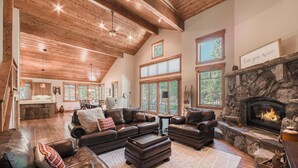 A spacious living room with leather sofas, a stone fireplace, and large windows. - Monthly Lease - Freedom Lodge by Tahoe Getaways - 4BR Centrally Located w/ Bonus Room (Truckee)
