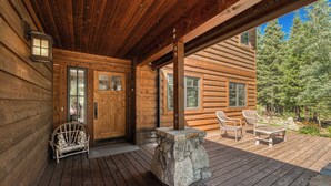 A wooden cabin with a porch, stone bench, wicker chairs, and a stone table. - Monthly Lease - Freedom Lodge by Tahoe Getaways - 4BR Centrally Located w/ Bonus Room (Truckee)