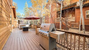 Una terrazza in legno con una griglia, posti a sedere all'aperto e una zona coperta con un ombrello rosso.