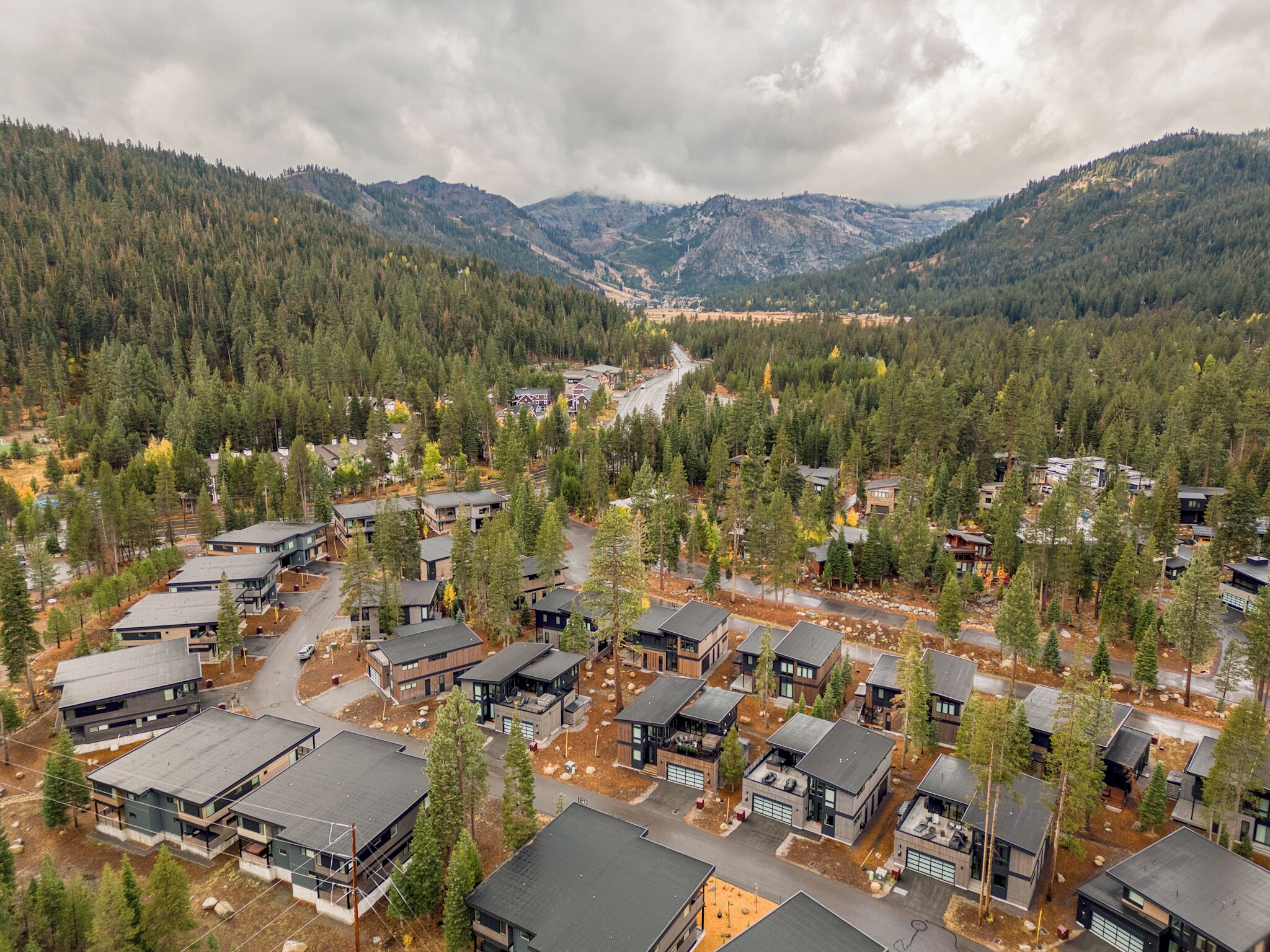 Una zona residencial con casas modernas, rodeada de bosques densos y montañas.