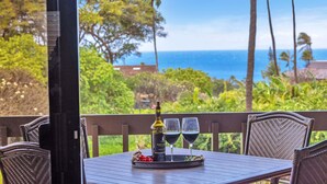 A table with a bottle and two glasses on a tray, overlooking a scenic view of the ocean and greenery. - Sunlit 2BR Island Haven Plantation Style (Lahaina)