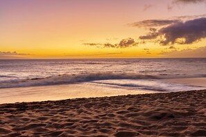 Une plage de sable avec des vagues au coucher du soleil.