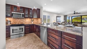 A modern kitchen with dark wooden cabinets, stainless steel appliances, and a granite countertop. - Sunlit 2BR Island Haven Plantation Style (Lahaina)
