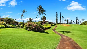 A golf course with a pathway, palm trees, and a building in the background. - Sunlit 2BR Island Haven Plantation Style (Lahaina)