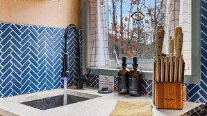 A kitchen with a herringbone tile backsplash, a window with a view of trees, a sink, and a knife block. - The Nook - Cozy Bungalow in the Countryside (Weaverville)