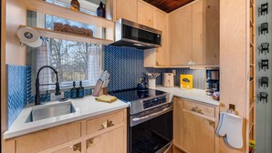 A modern kitchen with wooden cabinets, a stainless steel microwave, and a built-in oven. - The Nook - Cozy Bungalow in the Countryside (Weaverville)