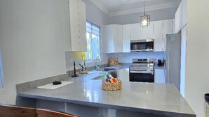 A modern kitchen with a central island, stainless steel appliances, and wooden chairs. - Choose To Be Happy @ SkyView #3 (Kingston)