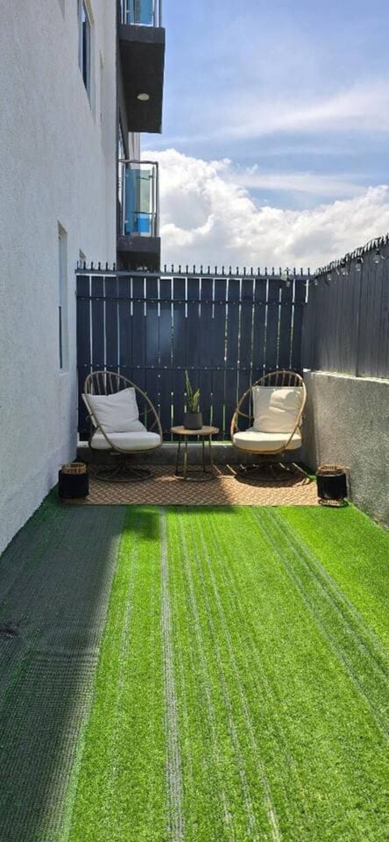 A small outdoor patio with two wicker chairs, a small table, and a view of a building.