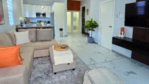 A living room with a sectional sofa, a flat-screen TV, a dining area, and a kitchen in the background. - Choose To Be Happy @ SkyView #3 (Kingston)