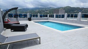 A rooftop pool with lounge chairs, a small table, and a view of the surrounding landscape. - Choose To Be Happy @ SkyView #3 (Kingston)