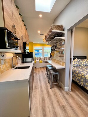 A compact kitchen with a built-in oven, a dining area with a bench, and a bed with a patterned bedspread.