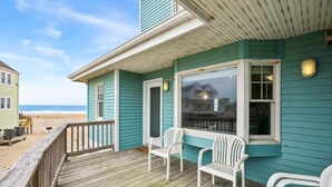 Una casa sulla spiaggia con veranda in legno, due sedie bianche e vista sull'oceano.