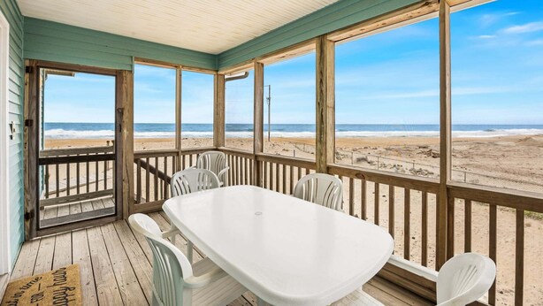 Una terrazza riparata con tavolo e sedie, con vista sulla spiaggia.