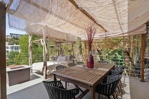 Un patio al aire libre con una mesa y sillas de madera, un área de estar con cojines y un jarrón decorativo.
