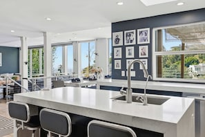 A modern kitchen with a central island, bar stools, a large window with a view, and framed pictures on the wall.
