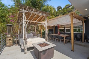 Ein überdachter Außenbereich mit Tisch und Stühlen, einer Steintonne und einer Pergola.