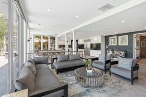 Ein modernes Interieur mit einer Couch, Sesseln, einem Couchtisch und einem Essbereich, der durch große Fenster sichtbar ist.