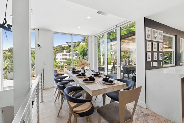 Un comedor con una mesa larga dispuesta para seis personas, ventanas amplias y vistas de los edificios circundantes.