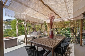 Un patio al aire libre con una mesa y sillas de madera, un área de estar con cojines y un jarrón decorativo.