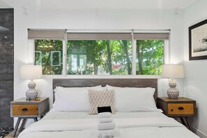 A bedroom with a bed, two nightstands, a window with a view of trees, and a framed picture on the wall.