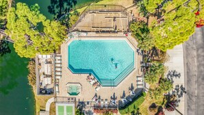 Ein achteckiger Pool mit umlaufender Terrasse, ein Tennisplatz und ein Parkplatz.
