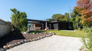 Et moderne hus i to etager med en overdækket terrasse, grusindkørsel og en anlagt have.