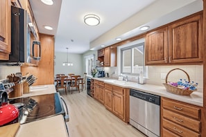 A modern kitchen with wooden cabinets, stainless steel appliances, and a dining area with a table and chairs. - Cozy fully remodeled home in Hermitage. (Hermitage)
