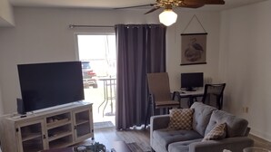 A living room with a flat-screen TV, a ceiling fan, a sofa, a coffee table, and a dining area with chairs and a table. - Charming 2-bedroom condo with AC in Biloxi breeze (Biloxi)