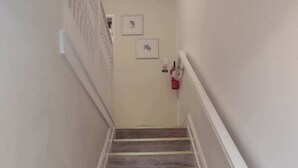 A staircase with wooden steps and white railings, leading to a room with a door and a wall-mounted fire extinguisher. - Charming 2-bedroom condo with AC in Biloxi breeze (Biloxi)