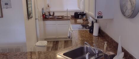 A kitchen with a granite countertop, stainless steel sink, and a clock on the wall.