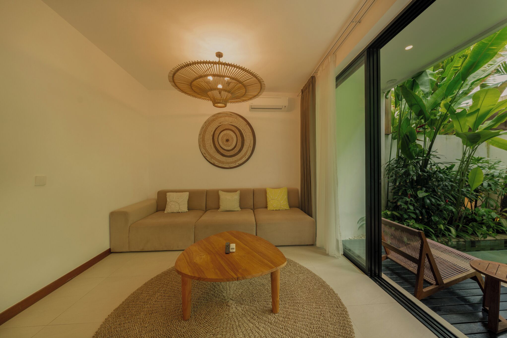 Un salon comprenant un canapé, une table basse, un luminaire fixé au mur et donnant sur un balcon agrémenté de plantes.